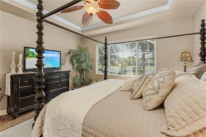 Primary bedroom with ensuite bathroom, tray ceiling with crown molding, and shiplap accent wall. Offers views of the lake and pool.