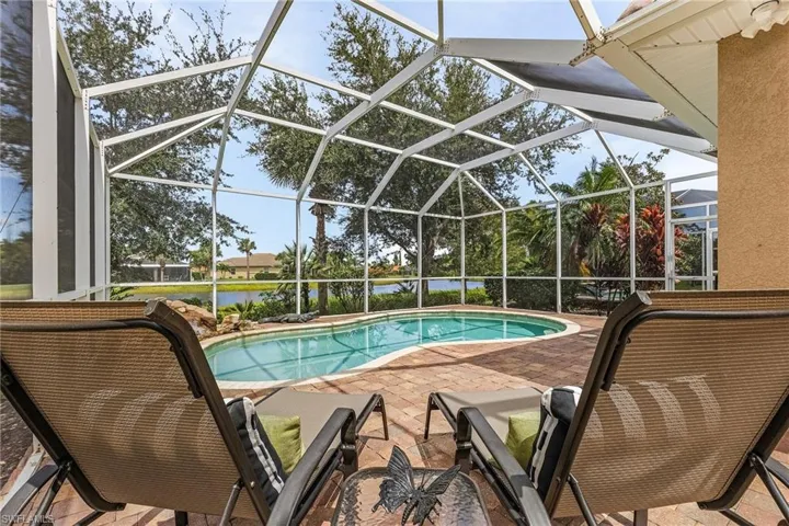 View of the swimming pool featuring a newer screen enclosure, complemented by a serene lake view and a welcoming patio area.