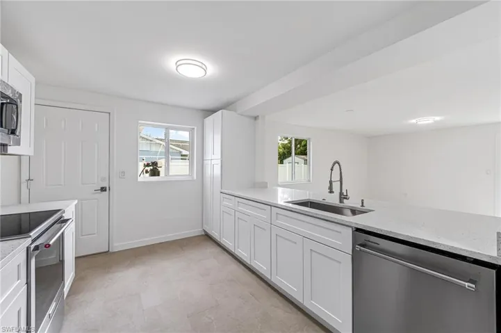 Kitchen featuring sink, stainless steel appliances, white cabinets, and light stone countertops