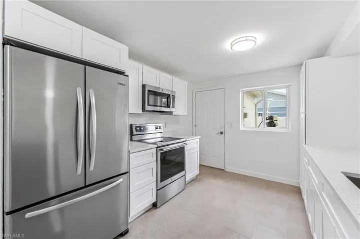 Kitchen with white cabinetry, light stone countertops, and appliances with stainless steel finishes
