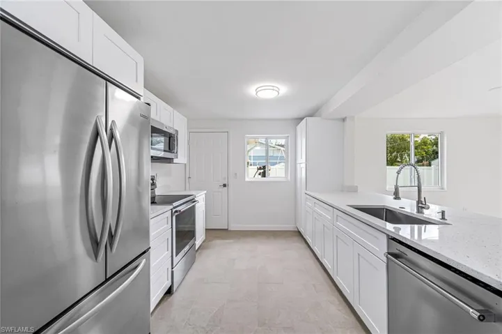 Kitchen featuring sink, white cabinetry, light stone counters, and appliances with stainless steel finishes