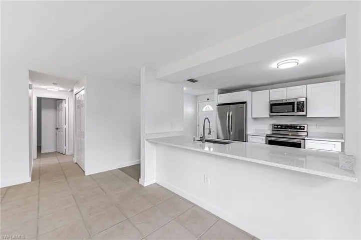 Kitchen featuring light stone countertops, white cabinetry, stainless steel appliances, sink, and kitchen peninsula