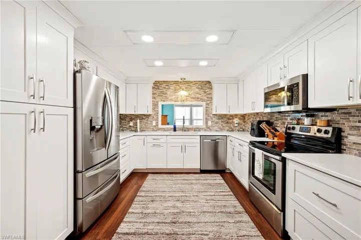 Kitchen featuring appliances with stainless steel finishes, a sink, dark wood-style flooring, tasteful backsplash, and recessed lighting