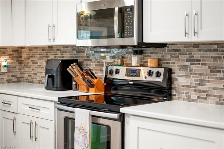 Kitchen with stainless steel appliances, tasteful backsplash, white cabinetry, and light countertops