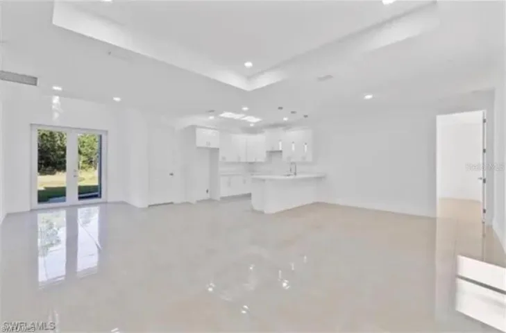 Open-concept interior featuring high tray ceilings, polished tile flooring, recessed lighting, white cabinetry, and glass-paneled double doors