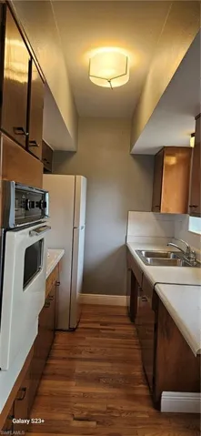 Kitchen featuring light countertops, oven, dark wood-style flooring, and refrigerator