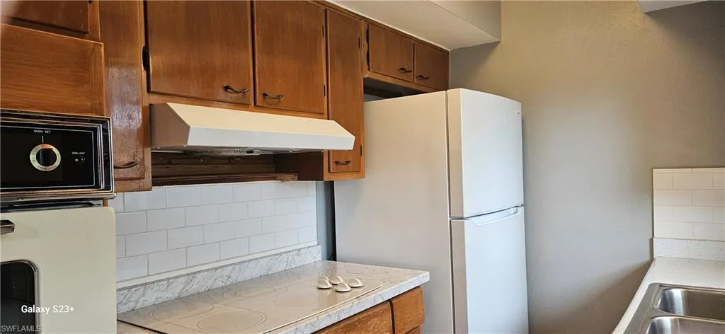 Kitchen with brown cabinetry, light countertops, tasteful backsplash, electric cooktop, and under cabinet range hood