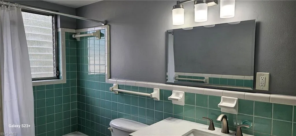 Bathroom featuring tiled shower, vanity, plenty of natural light, a textured wall, and tile walls