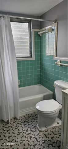 Full bath with shower / bath combo with shower curtain, tile walls, vanity, and a wainscoted wall