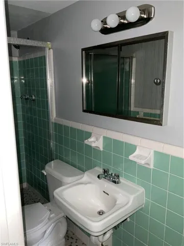 Full bathroom featuring a stall shower, tile walls, and wainscoting