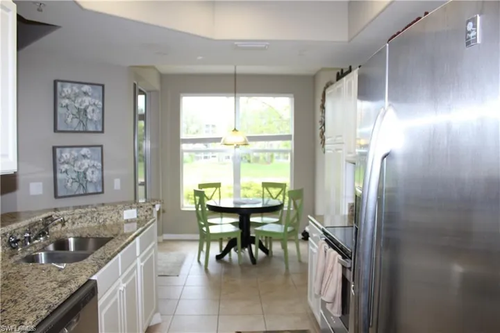 Kitchen with light tile patterned floors, white cabinets, stainless steel appliances, light stone countertops, and sink