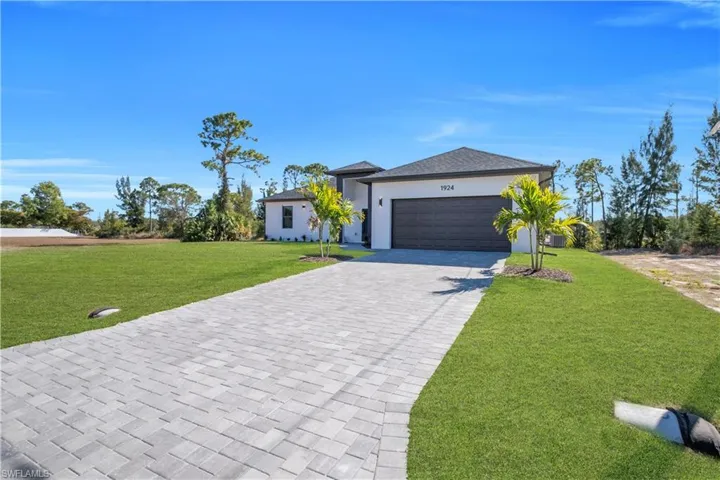 View of front of house with a front lawn, decorative driveway, an attached garage, and stucco siding