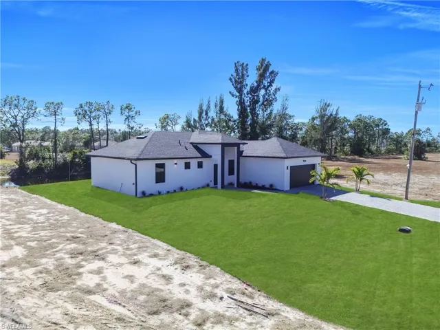 View of front of home with stucco siding, driveway, a front yard, and roof with shingles