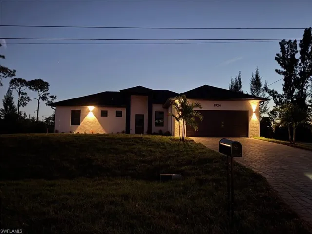 View of front facade featuring decorative driveway, stucco siding, a garage, and a front yard