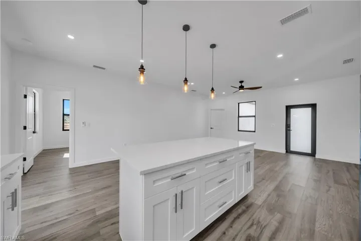 Kitchen featuring decorative light fixtures, a kitchen island, white cabinets, open floor plan, and light wood finished floors