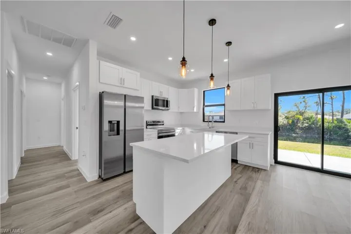 Kitchen with stainless steel appliances, white cabinetry, decorative light fixtures, a center island, and light wood-style flooring