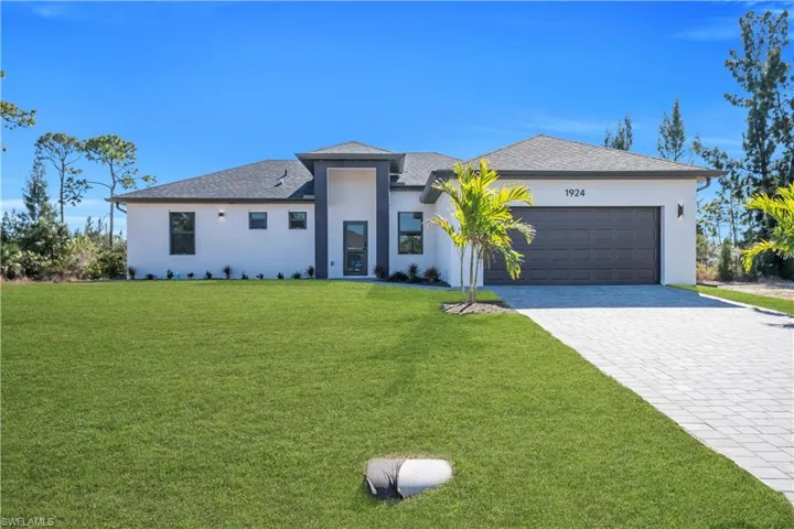 Prairie-style home featuring a front yard, stucco siding, decorative driveway, an attached garage, and roof with shingles
