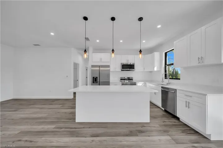 Kitchen with stainless steel appliances, white cabinetry, hanging light fixtures, and a center island