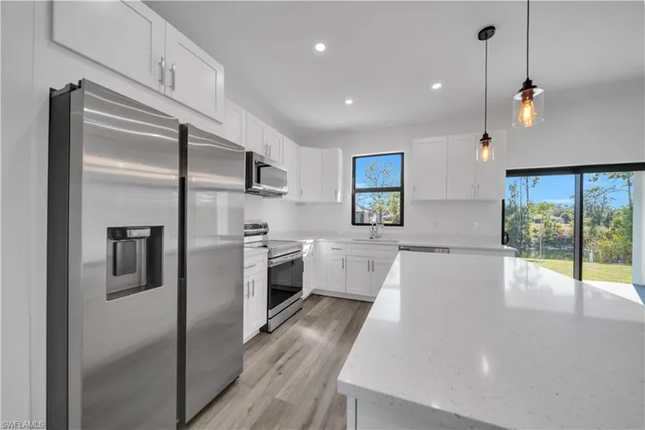 Kitchen with stainless steel appliances, hanging light fixtures, white cabinets, light stone counters, and light wood-type flooring