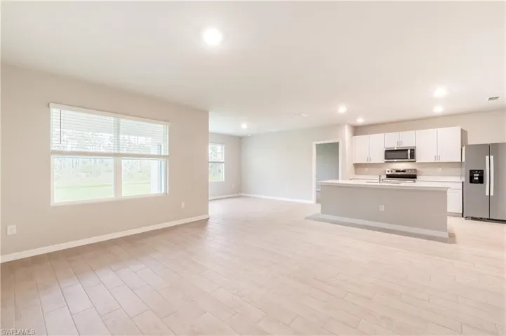Kitchen featuring appliances with stainless steel finishes, white cabinetry, a kitchen island with sink, light countertops, and open floor plan