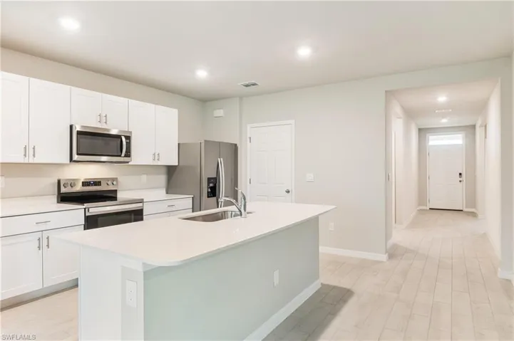 Kitchen with stainless steel appliances, an island with sink, white cabinets, light wood-style floors, and recessed lighting