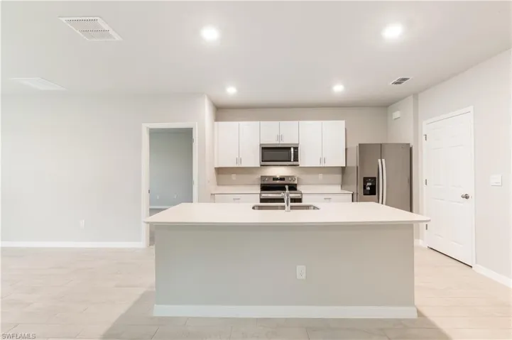 Kitchen featuring appliances with stainless steel finishes, white cabinetry, an island with sink, recessed lighting, and light wood finished floors