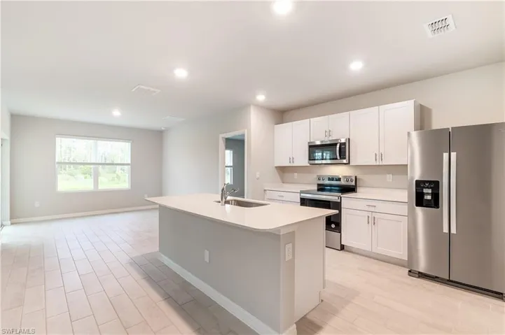 Kitchen with stainless steel appliances, light wood-type flooring, recessed lighting, a center island with sink, and white cabinetry