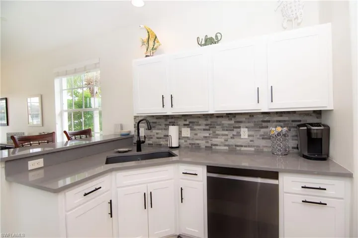 Kitchen featuring bright white Shaker style cabinetry with modern hardware, gray quartz countertops, stainless steel appliances, tile backsplash, recessed lighting and light tile floors.