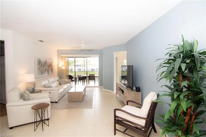 Tastefully furnished living room with ceiling fan and light tile floors with telescoping sliding doors to the screened lanai.