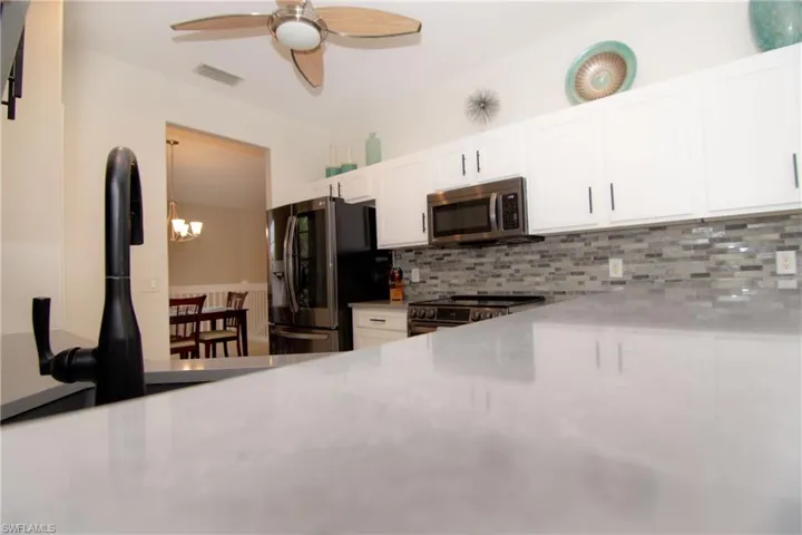 Kitchen featuring bright white Shaker style cabinetry with modern hardware, gray quartz countertops, stainless steel appliances, tile backsplash, recessed lighting and light tile floors.