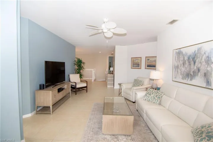 Tastefully furnished living room with ceiling fan and light tile floors with telescoping sliding doors to the screened lanai.