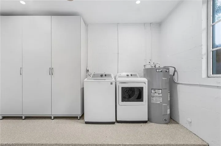 Laundryroom with electric water heater, independent washer and dryer, and concrete block wall