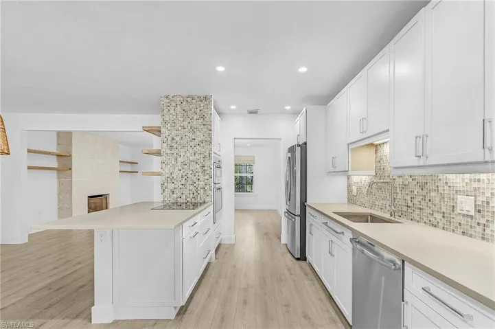 Kitchen with appliances with stainless steel finishes, decorative backsplash, light wood-style flooring, light countertops, and white cabinets