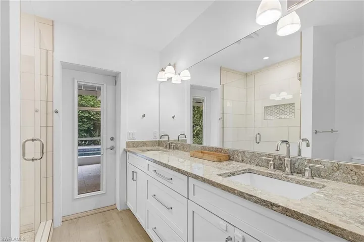 Full bath featuring double vanity and a standing shower, with a door leading to the lanaii and pool