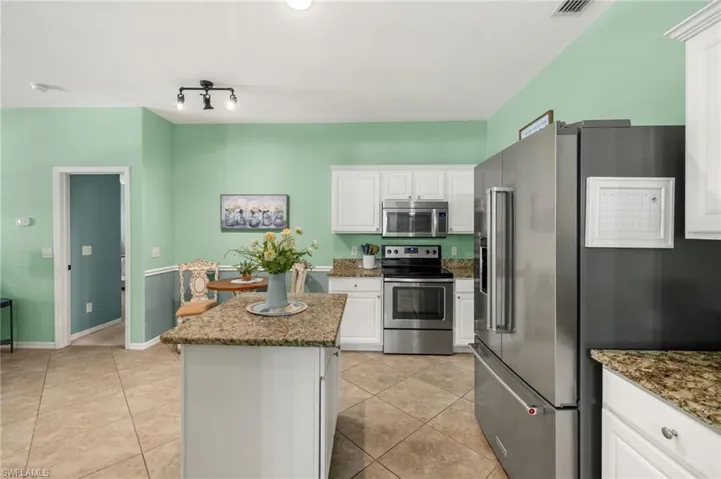 Kitchen with stainless steel appliances, a center island, light tile patterned floors, and stone countertops