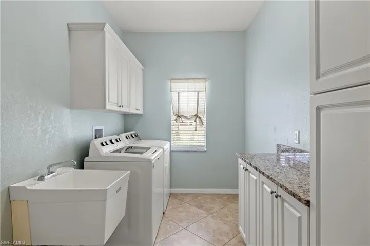 Washroom with light tile patterned flooring, washer and clothes dryer, sink, and cabinets