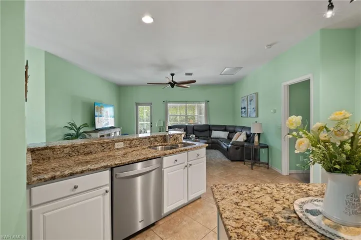 Kitchen with white cabinetry, light tile patterned flooring, ceiling fan, stone counters, and dishwasher
