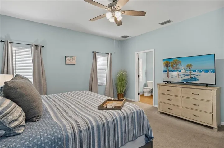 Bedroom featuring multiple windows, ensuite bath, light colored carpet, and ceiling fan