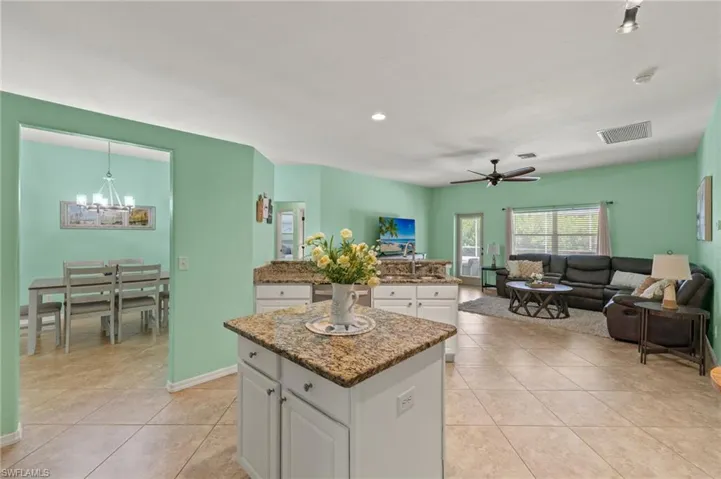 Kitchen featuring light tile patterned floors, white cabinets, ceiling fan with notable chandelier, a center island, and pendant lighting