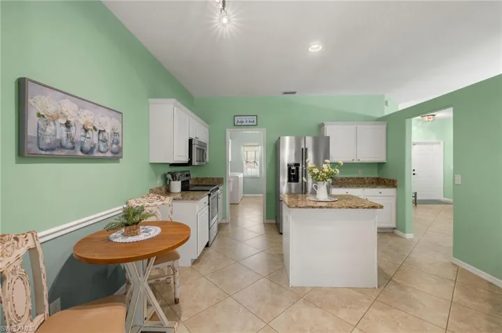 Kitchen with stainless steel appliances, stone counters, white cabinets, a center island, and light tile patterned floors