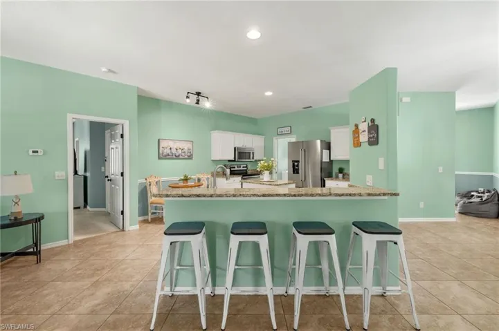 Kitchen with appliances with stainless steel finishes, white cabinetry, light stone countertops, and light tile patterned flooring