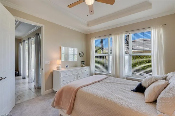 Bedroom with ornamental molding, ceiling fan, multiple windows, light carpet, and a tray ceiling