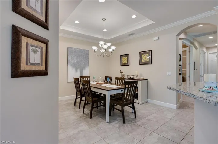 Dining area featuring crown molding, arched walkways, a chandelier, light tile patterned floors, and a raised ceiling
