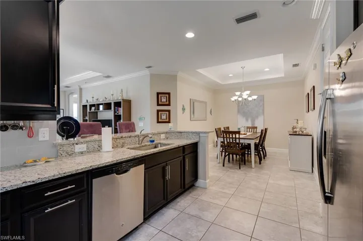 Kitchen featuring ornamental molding, a tray ceiling, light stone counters, stainless steel appliances, and a peninsula