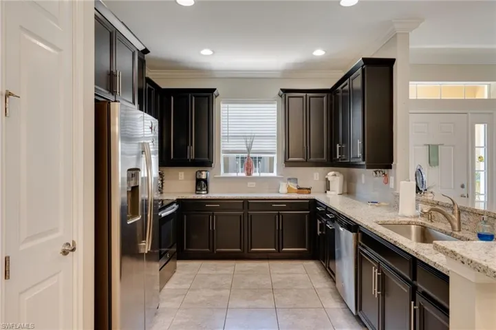 Kitchen with stainless steel appliances, light stone counters, crown molding, light tile patterned flooring, and backsplash