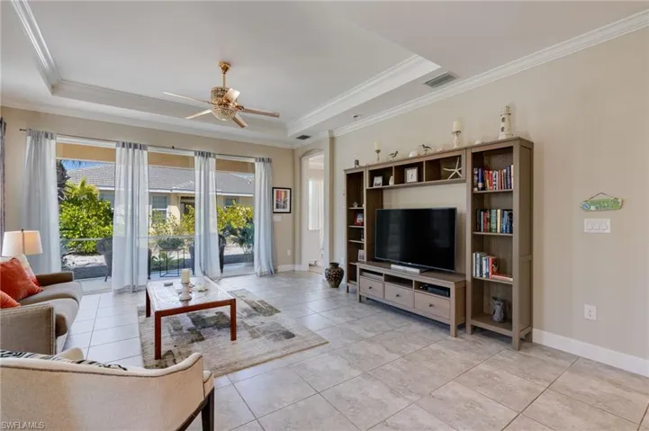 Living room with a ceiling fan, a tray ceiling, and crown molding