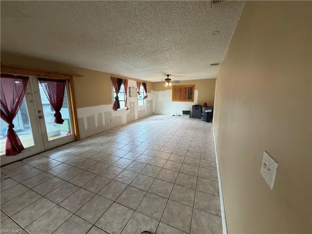 Large interior space featuring ceramic tile flooring, dual glass-paneled patio doors, multiple windows, and a ceiling-mounted light fixture