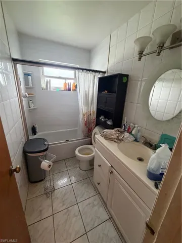Full-wall ceramic tile, vanity with integrated basin, oval wall-mounted mirror, three-light fixture, and ceramic tile flooring