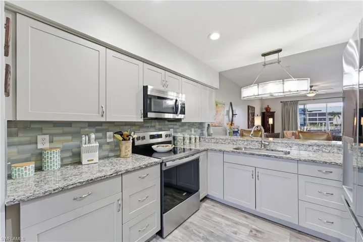 Kitchen with stainless steel appliances, light stone counters, a ceiling fan, decorative light fixtures, and light wood-style flooring