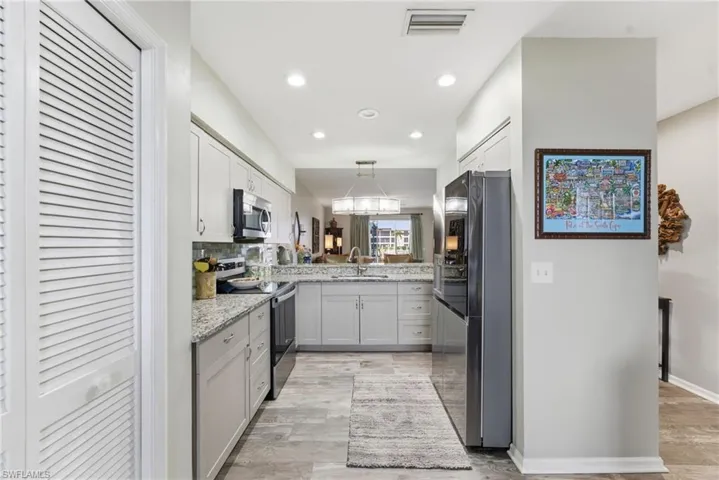 Kitchen featuring stainless steel appliances, light stone countertops, white cabinets, and decorative light fixtures